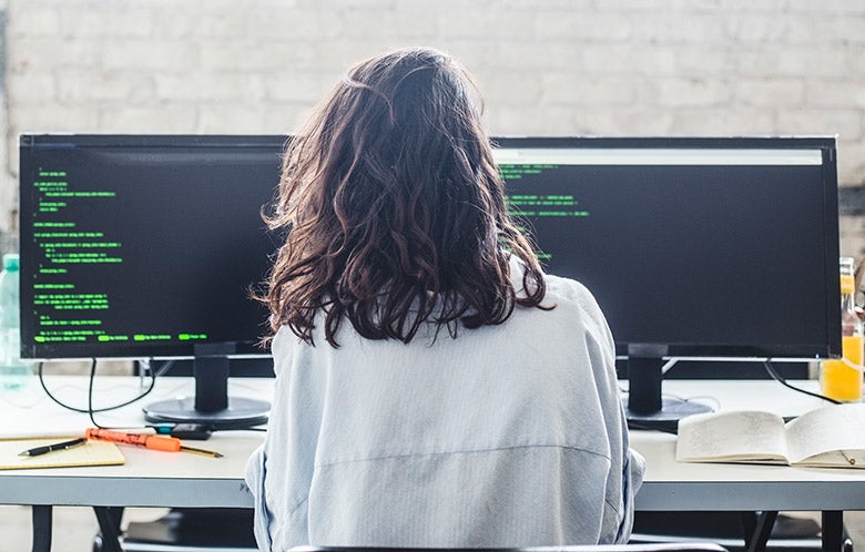 Rear view of female computer developer coding at desk