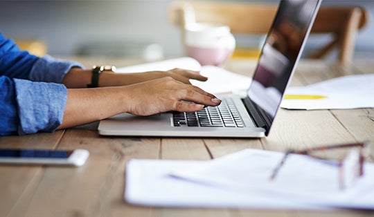 Handen werkend aan een laptop die op een bureau staat