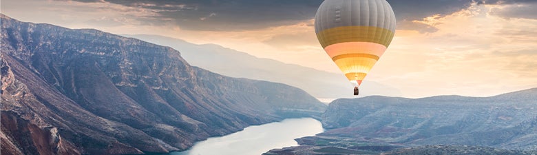 Hot air balloon in the sky over a river running through a canyon.