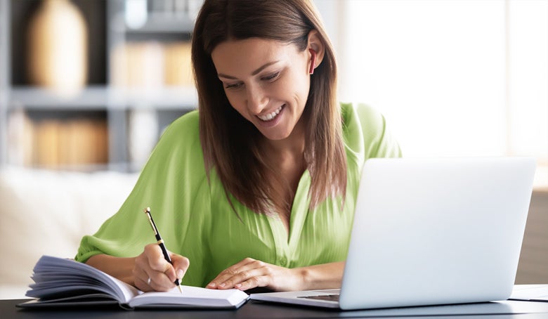 A woman taking notes while on her laptop at a desk