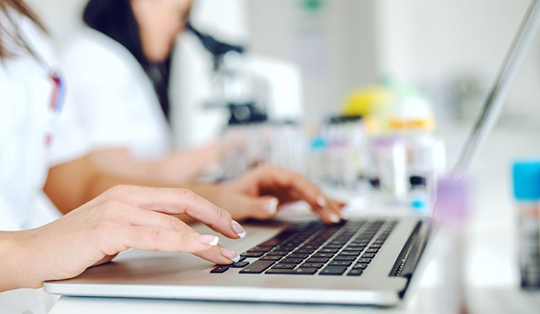 Medical researcher in white uniform sitting in lab and using laptop while working