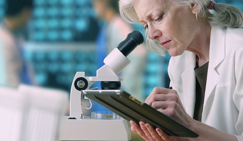 medical researcher taking notes on tablet computer in busy lab